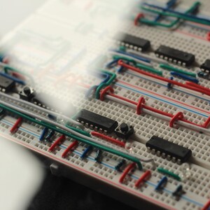Op de afbeelding: Close-up van een breadboard met ge&iuml;ntegreerde circuits, draden en knoppen. De draden zijn rood, blauw, groen en wit, waardoor een complex netwerk ontstaat. De componenten zijn gerangschikt op een witte kunststof basis.