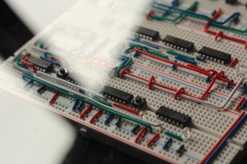 Op de afbeelding: Close-up van een breadboard met ge&iuml;ntegreerde circuits, draden en knoppen. De draden zijn rood, blauw, groen en wit, waardoor een complex netwerk ontstaat. De componenten zijn gerangschikt op een witte kunststof basis.