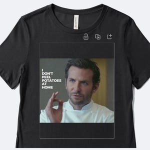 May include: Black t-shirt featuring a rectangular image of a man in a chef's coat. The image includes the text "I DON'T PEEL POTATOES AT HOME". The man is making an "okay" hand gesture.