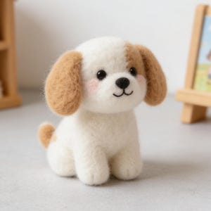 Peut inclure: Figurine de chien en feutre fait à la main, avec un corps blanc, des oreilles marron et une petite queue marron. Le chien a un nez noir, des joues roses et est assis. Une petite étagère en bois et une image encadrée sont en arrière-plan.