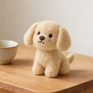 Peut inclure: Un jouet en feutre jaune clair en forme de chien, avec des oreilles tombantes, une petite queue et un visage souriant. Le jouet a des yeux noirs et un nez brun, et est posé sur une table en bois à côté d'un petit bol en céramique.