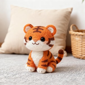 May include: A handcrafted orange and brown felt tiger figurine with black eyes and a smiling mouth. The tiger has brown stripes and white accents on its face, paws, and belly. The plush toy is sitting on a gray carpet.