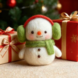 Pode incluir: Uma figura de boneco de neve artesanal com protetores de ouvido, cachecol e chapéu vermelhos. O boneco de neve tem um nariz de cenoura, bochechas rosadas e olhos de botão marrons. Dois presentes embrulhados com fitas vermelhas e douradas estão ao fundo, com uma árvore de Natal.