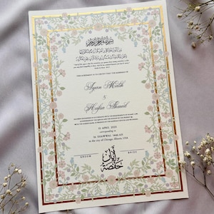 May include: A wedding certificate with floral border in soft pink, blue, and green. The document features gold accents and elegant calligraphy with the names Ayan Malik and Hafsa Ahmed, along with the date April 15, 2025, and location.