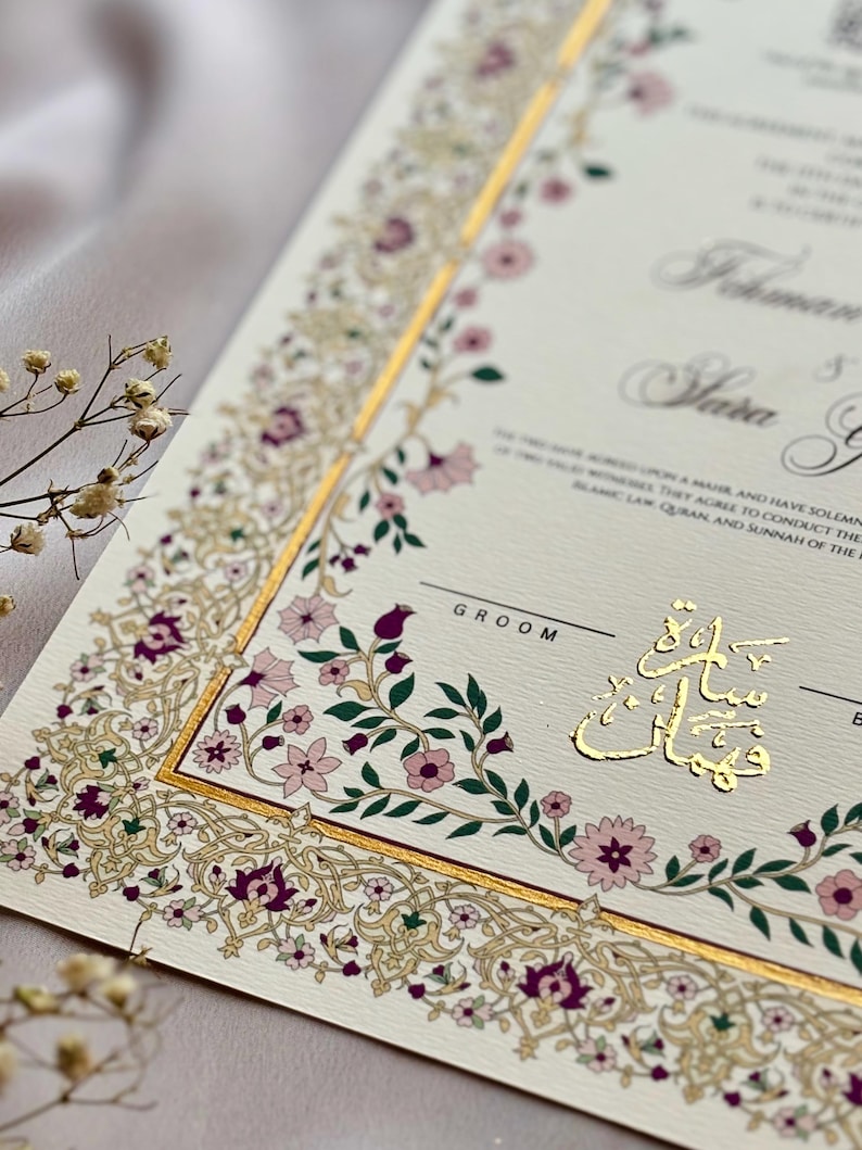 Puede incluir: Invitaci&oacute;n de boda marfil con detalles dorados y borde floral en tonos rosa y morado. La invitaci&oacute;n presenta caligraf&iacute;a elegante y texto en idioma extranjero.