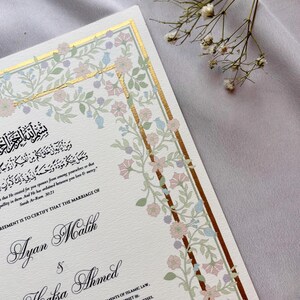 May include: Elegant wedding invitation with floral border in soft pink, blue, and green hues. The invitation features gold accents and calligraphy with the names Ayan Malik and Hafsa Ahmed, and the date April 15, 2025.