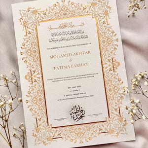 May include: Ivory wedding certificate with gold ornate border and text. The certificate reads "This agreement is to certify the marriage of Mohamed Akhtar & Fatima Farhat" with Arabic script at the top and bottom. The date is 31st May 2025.