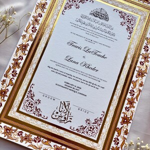 Może przedstawiać: Eleganckie zaproszenie ślubne ze złotymi akcentami i ozdobnymi kwiatowymi obramowaniami. Zaproszenie zawiera nazwiska Travis La Touche i Lana Kheder, arabski skrypt oraz datę 14 lutego 2026.