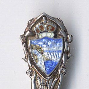 May include: Silver souvenir spoon with a blue and white enamel design of a waterfall and a crown. The spoon handle is decorated with a stylized figure.