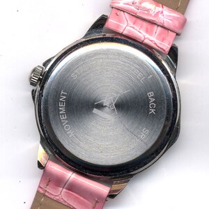 May include: The back of a silver wristwatch with a pink leather band. The watch face has the words "Steel Back" and "Movement" engraved on it.