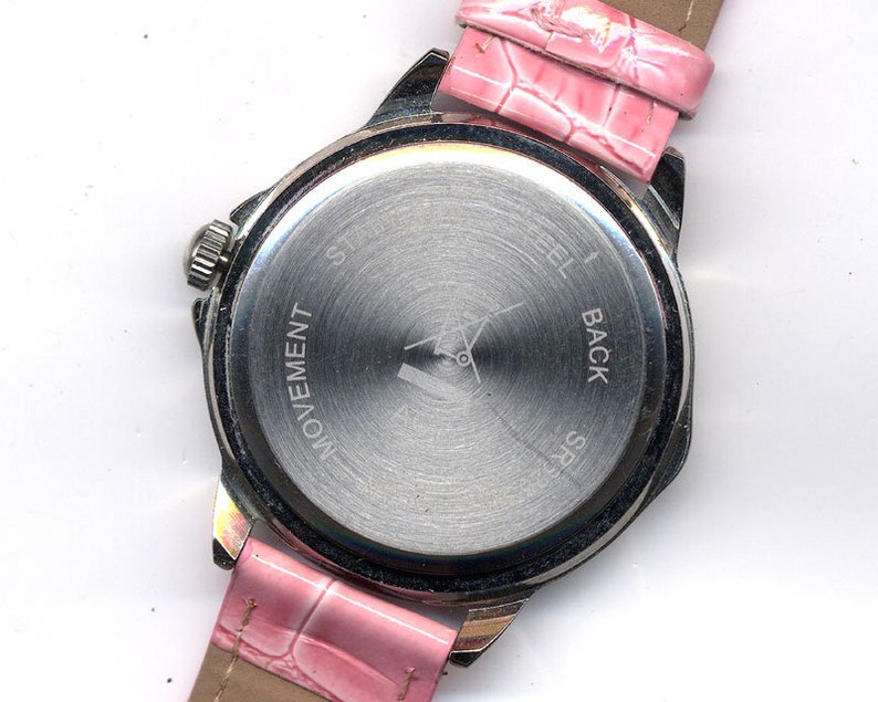 May include: The back of a silver wristwatch with a pink leather band. The watch face has the words "Steel Back" and "Movement" engraved on it.