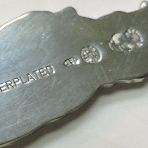 May include: Close-up of the back of a silver-plated object with the words "SILVERPLATED" stamped on the surface.