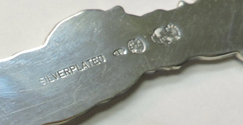 May include: Close-up of the back of a silver-plated object with the words "SILVERPLATED" stamped on the surface.
