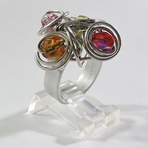 May include: A silver ring with three colourful glass beads wrapped in wire. The beads are orange, pink and red.