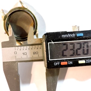May include: A silver watch case being measured with a digital caliper. The caliper reads 23.20 mm.
