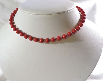 May include: A red beaded necklace on a white mannequin bust. The necklace is made of round beads and is approximately 16 inches long.