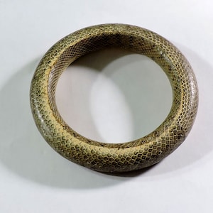 Peut inclure: Un bracelet en peau de serpent marron. Le bracelet est fait de véritable peau de serpent et a une surface texturée.