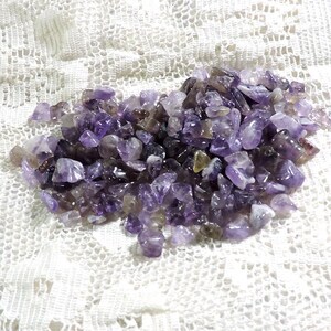 May include: A pile of small, purple amethyst chips. The chips are irregularly shaped and have a natural, rough texture.
