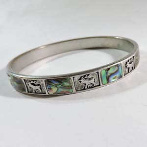 May include: A silver bangle bracelet with a decorative design featuring abalone shell inlays and stylized deer figures.