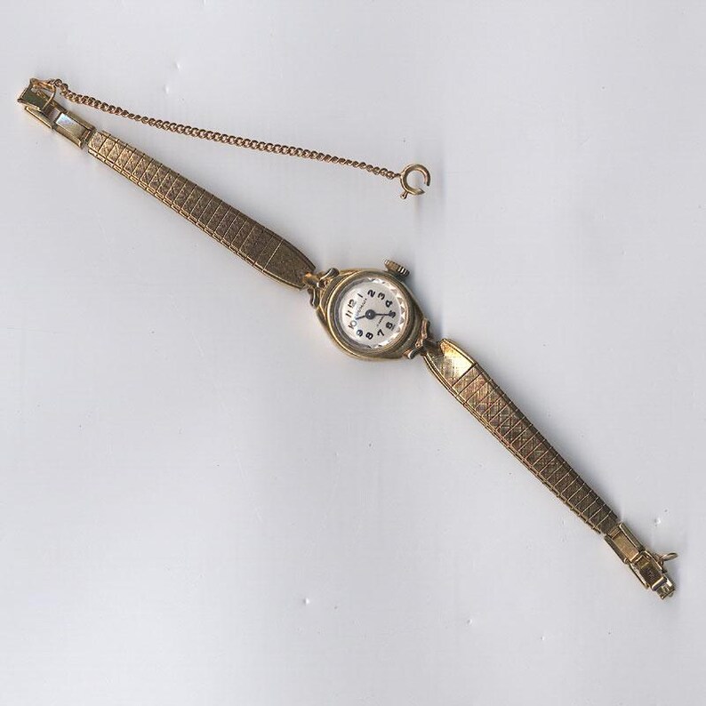 K&ouml;nnte beinhalten: Eine goldfarbene Armbanduhr mit wei&szlig;em Zifferblatt und schwarzen r&ouml;mischen Ziffern. Die Uhr hat ein goldfarbenes Metallband mit einer Kette.