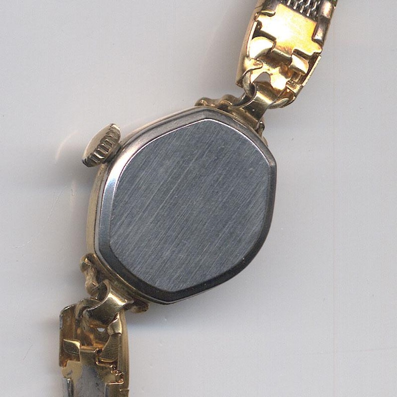K&ouml;nnte beinhalten: Goldfarbene Armbanduhr mit einem runden, silberfarbenen Geh&auml;useboden. Die Uhr hat ein goldfarbenes Metallband.