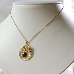 May include: A gold chain necklace with a pendant featuring a green gemstone surrounded by delicate gold wirework.