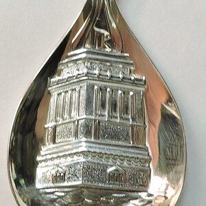 May include: Silver spoon with a detailed embossed image of a building and the text "1886-1986".