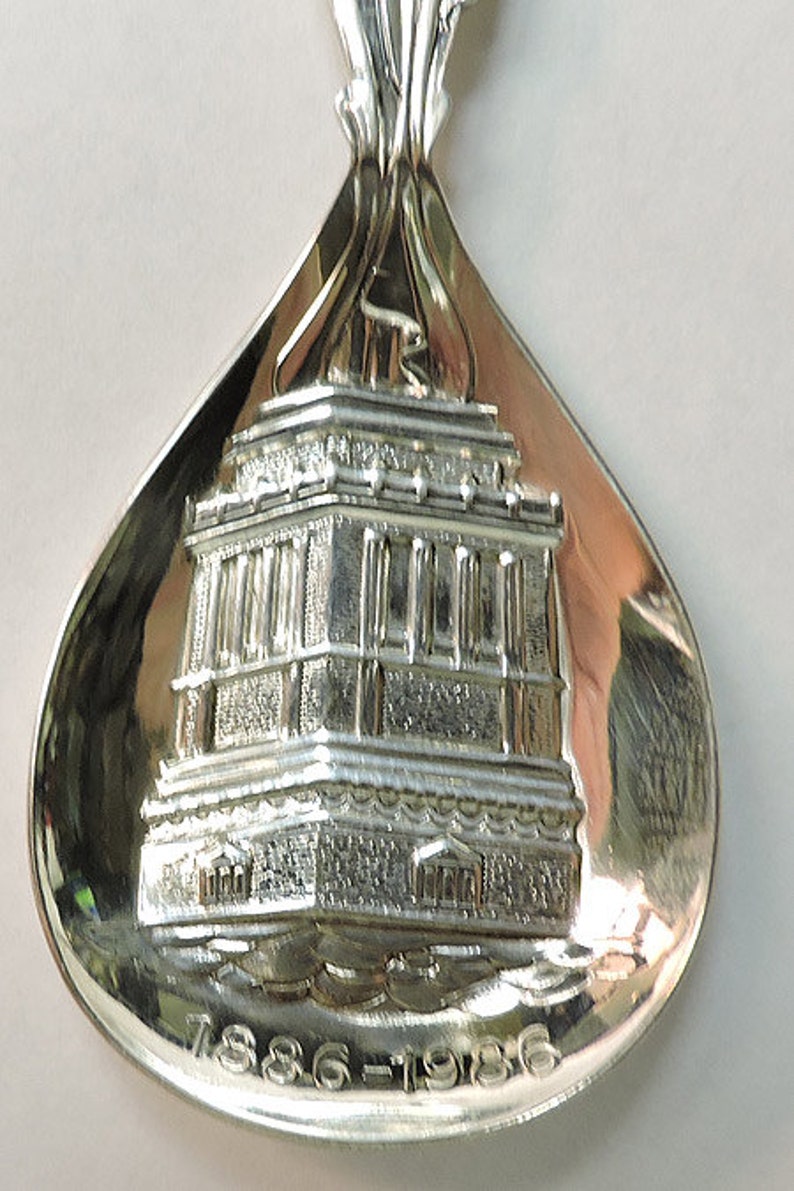 May include: Silver spoon with a detailed embossed image of a building and the text "1886-1986".