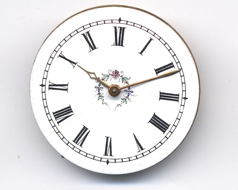 May include: A white clock face with black Roman numeral hour markers and black minute markers. The clock hands are gold and the center of the clock face has a floral design.