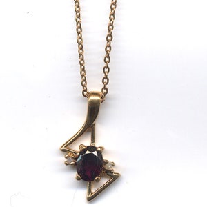 May include: A gold chain necklace with a pendant featuring a dark purple gemstone surrounded by smaller clear gemstones.