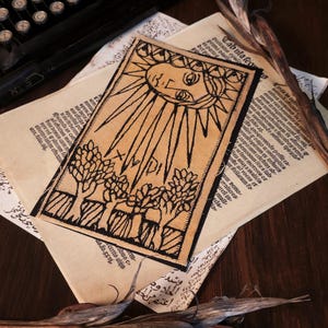 Puede incluir: Una tarjeta de tarot beige con un diseño de sol negro y el texto "XMPDI". La tarjeta presenta un sol con rayos y árboles en la parte inferior. La tarjeta está sobre papeles viejos.