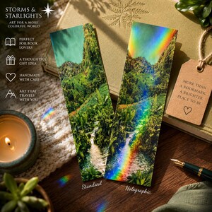 May include: Two rectangular bookmarks featuring a vibrant landscape illustration of a lush green forest with a flowing stream. One bookmark has a standard finish, while the other displays a holographic rainbow light effect.