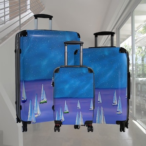 May include: Set of three rolling suitcases with a blue and purple design featuring white sailboats and a starry sky. The luggage has black accents, telescoping handles, and four wheels for easy maneuverability. The suitcases are different sizes.