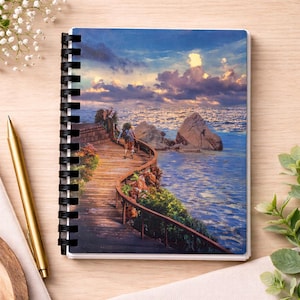 Puede incluir: Cuaderno con espiral con una imagen escénica de un paseo marítimo de madera sobre el océano bajo un cielo nublado. El cuaderno tiene una encuadernación en espiral negra y un borde blanco. Un bolígrafo dorado descansa junto al cuaderno.