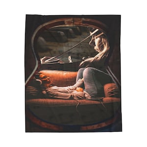 May include: A blanket featuring a double exposure image. One image shows a person playing a violin, and the other shows a person wearing headphones lying on a couch. The blanket has a dark brown border.