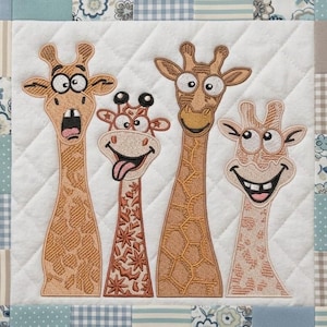 Pode incluir: Um quadrado acolchoado com quatro girafas de desenho animado com rostos expressivos. As girafas são em tons de castanho e bege, com detalhes bordados. O fundo é branco com um padrão de losangos, rodeado por uma borda de retalhos em azul e bege.