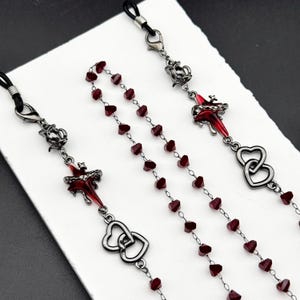 Op de afbeelding: Brillenkettingen met decoratieve elementen. Eén ketting heeft een streng kleine, rode, hartvormige kralen. Andere kettingen hebben sierlijke metalen bedels in rood en zilver, waaronder harten en bloemmotieven.