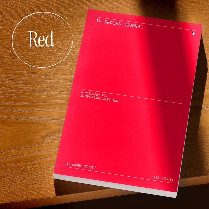 Op de afbeelding: Een felrood notitieboek met de tekst "TV SERIES JOURNAL" en "A NOTEBOOK FOR INTENTIONAL WATCHING." De kaft bevat ook "BY K&Uuml;&Ntilde;EL STUDIO" en "(120 PAGES)." Het notitieboek ligt op een houten oppervlak.