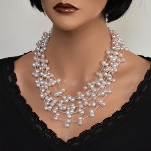 May include: A multi-strand pearl necklace with a graduated design. The necklace is made of white and blush pink pearls and is layered in a cascading style.