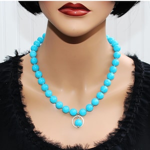 May include: A turquoise beaded necklace with a silver pendant. The necklace features large, round beads in a vibrant blue-green hue. The pendant is a small turquoise bead suspended within a silver circle. The necklace is displayed on a mannequin.