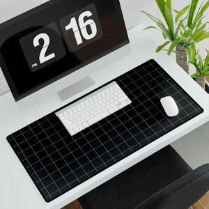 May include: A black desk mat with a white grid pattern, a white keyboard and mouse. A computer monitor displays the time as 2:16 PM. A green plant is in the background.