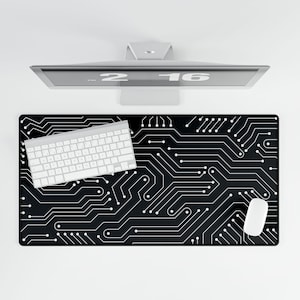 May include: A black rectangular desk mat featuring a white circuit board pattern. A white keyboard and mouse are on the mat. A silver computer monitor is above the mat.