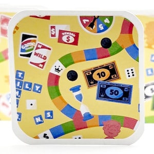 May include: A collection of square, yellow plates with rounded corners, each decorated with a board game design. The plates feature dice, money, and game cards in a colourful arrangement. They are set against a white backdrop.