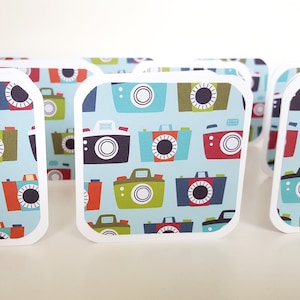 May include: A set of eight blank cards with a white border and a blue background featuring a repeating pattern of colorful cameras.