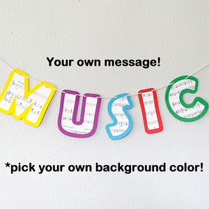 May include: A colorful banner with the word "MUSIC" spelled out in large letters. Each letter is made of sheet music and outlined in a different color. The banner is hanging from a white string against a white wall. The text "Your own message!" and "*pick your own background color!" are also visible.