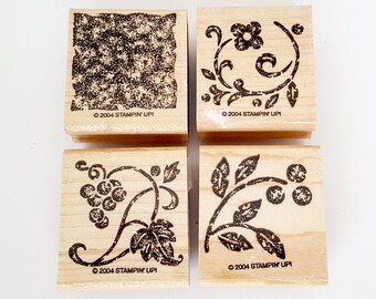 Peut inclure: Ensemble de quatre tampons en caoutchouc sur bois avec des motifs floraux et de vignes. Les tampons sont tous carrés et ont une base en bois brun. Les motifs sont en encre noire et comprennent une vigne de raisin, un motif de coin floral et un motif texturé.
