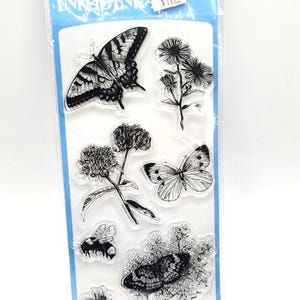 May include: Clear stamps set featuring detailed black and white illustrations of butterflies, flowers, and insects. The package includes the brand name "INKADINKA" and the text "7 PC / PZ".
