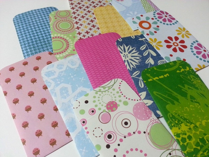 May include: A collection of colorful patterned paper envelopes with rounded corners. The envelopes feature various designs, including polka dots, flowers, geometric shapes, and abstract patterns.