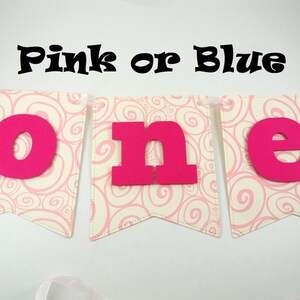 May include: Pink or Blue banner with the word "one" in large pink letters on a white background with a pink swirl pattern.