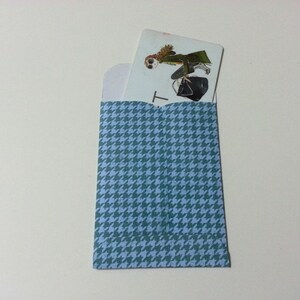 May include: A blue and white patterned envelope with a white card inside. The card has a drawing of a person wearing a green coat and a hat. The card has the letter "T" printed on it.